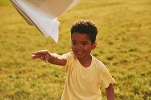 con avión de papel. niño afroamericano se divierte en el campo durante el día de verano foto