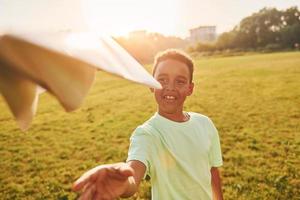 With paper plane. African american kid have fun in the field at summer daytime photo