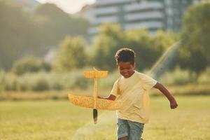 Playing with plane. African american kid have fun in the field at summer daytime photo