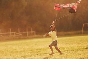 corriendo con cometa roja. niño afroamericano se divierte en el campo durante el día de verano foto