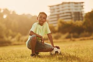 tomando un descanso. con balón de fútbol. niño afroamericano se divierte en el campo durante el día de verano foto