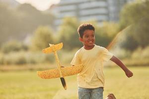 Playing with plane. African american kid have fun in the field at summer daytime photo