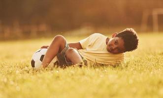 Taking a break. With soccer ball. African american kid have fun in the field at summer daytime photo