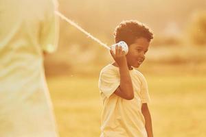 Having conversation by using cups on the knots. Two african american kids have fun in the field at summer daytime together photo