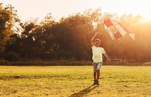 jugando con cometa. niño afroamericano se divierte en el campo durante el día de verano foto