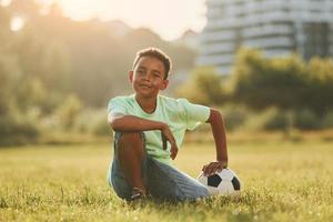 Taking a break. With soccer ball. African american kid have fun in the field at summer daytime photo