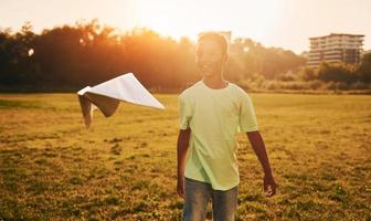 With paper plane. African american kid have fun in the field at summer daytime photo