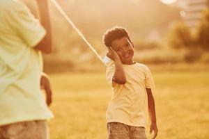 viejo teléfono de juguete. dos niños afroamericanos se divierten juntos en el campo durante el día de verano foto