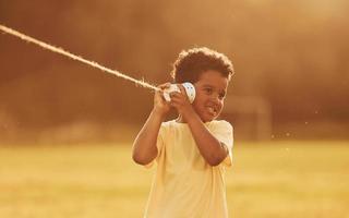 Talking by using cup on knot. African american kid have fun in the field at summer daytime photo