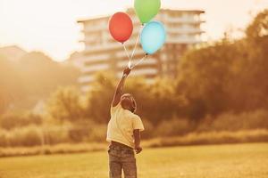 With balloons in hands. African american kid have fun in the field at summer daytime photo