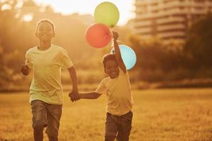 jugando con globos aerostáticos. dos niños afroamericanos se divierten juntos en el campo durante el día de verano foto