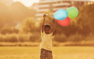 con globos en las manos. niño afroamericano se divierte en el campo durante el día de verano foto