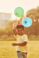 With balloons in hands. African american kid have fun in the field at summer daytime photo