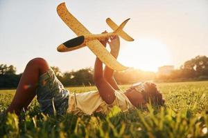 In glasses with toy plane. African american kid have fun in the field at summer daytime photo