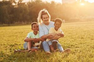 Adult woman sits with two black kids on the field at summer daytime photo