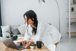 Wireless technology. Uses laptop. Woman in casual clothes is indoors at home photo