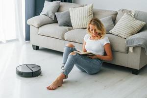 Blonde sits on the floor. Woman in casual clothes is indoors at home photo