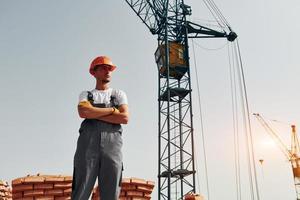 With crane at background. Young construction worker in uniform is busy at the unfinished building photo