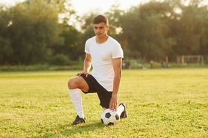 se sienta en la rodilla con la pelota. el joven futbolista tiene entrenamiento en el campo deportivo foto