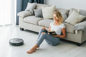 Blonde sits on the floor. Woman in casual clothes is indoors at home photo