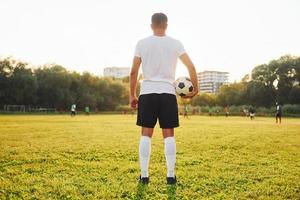 de pie y sosteniendo la pelota en la mano. el joven futbolista tiene entrenamiento en el campo deportivo foto