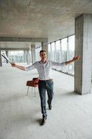 Near the chair. Young man in formal wear is working indoors on the construction photo