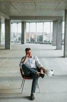 Talks by the phone. Young man in formal wear is working indoors on the construction photo