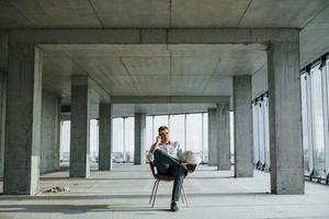 tener una conversación usando el teléfono. un joven con ropa formal está trabajando en el interior de la construcción foto