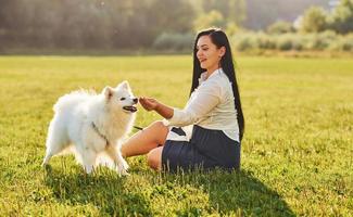 Woman is sitting on the ground of field with her cute dog photo