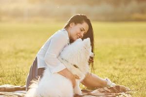 Beautiful woman in white shirt sitting with her dog on the field at sunny daytime photo