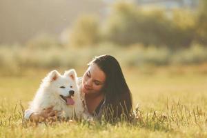 Laying down on the ground. Woman with her dog is having fun on the field at sunny daytime photo