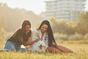 Two women with dog is having fun on the field at sunny daytime photo