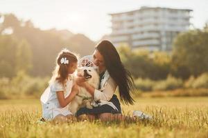 Playful mood. Woman and little girl have a walk with dog on the field at sunny daytime photo