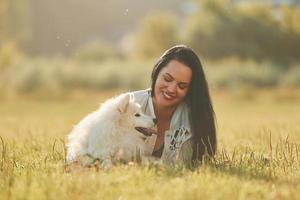 Laying down on the ground. Woman with her dog is having fun on the field at sunny daytime photo
