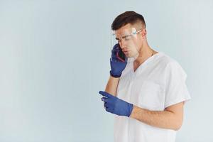 In white uniform. Young male doctor is indoors against white background photo