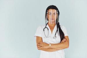 In protective face mask. Young female doctor in uniform is indoors photo