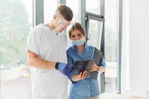 Looking at documents. Two doctors in uniform standing indoors and working together photo