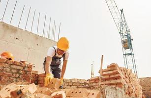 utilizando ladrillos. joven trabajador de la construcción en uniforme está ocupado en el edificio sin terminar foto