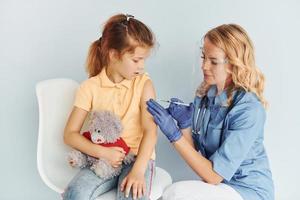 Holding teddy bear. Doctor in uniform making vaccination to the patient photo