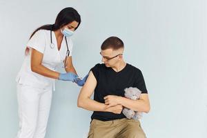 Man holding teddy bear during procedure. Doctor in uniform making vaccination to the patient photo