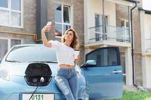 With phone. Young woman in casual clothes with her electromobile outdoors at daytime photo