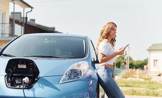 Standing near the car. Young woman in casual clothes with her electromobile outdoors at daytime photo