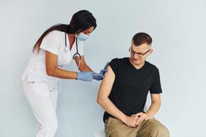 el hombre está nervioso. doctor en uniforme vacunando al paciente foto