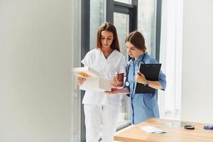 Looking at documents. Two doctors in uniform standing indoors and working together photo