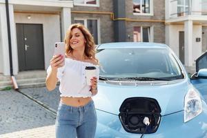 With phone. Young woman in casual clothes with her electromobile outdoors at daytime photo