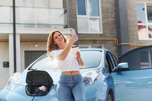 With phone. Young woman in casual clothes with her electromobile outdoors at daytime photo