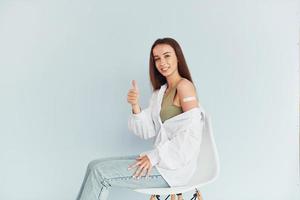 After vaccination. Young woman in white clothes sitting indoors against white background photo