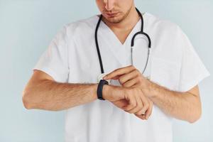 In white uniform. Young male doctor is indoors against white background photo