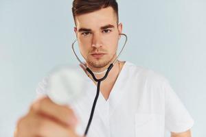 con estetoscopio joven médico masculino en uniforme está en el interior contra el fondo blanco foto