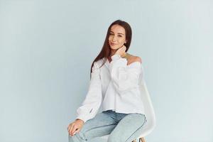 Young woman in white clothes sitting indoors against white background photo